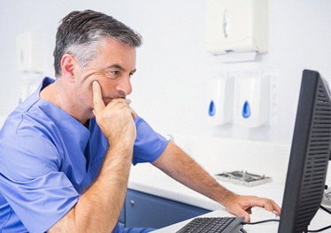 Dentist concentrating as he considers safety information on computer